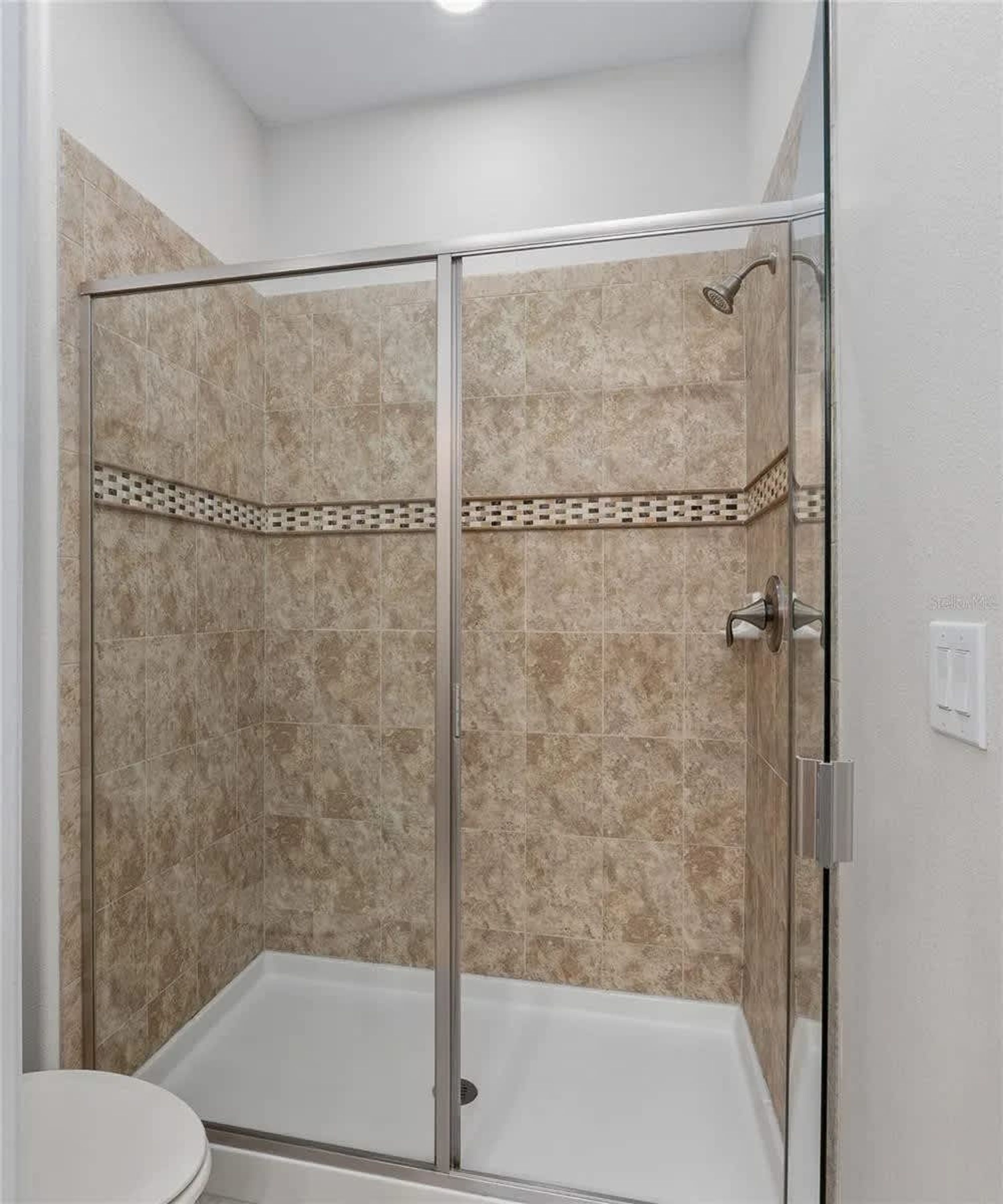 A walk-in shower with a glass door, beige tiles, and a small decorative tile border.