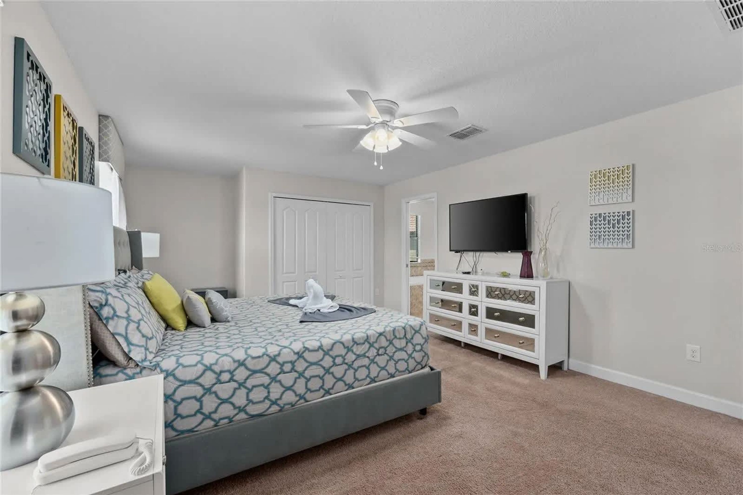 A bedroom with a bed, a dresser, a television, and a ceiling fan.
