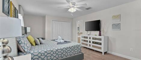 A bedroom with a bed, a dresser, a television, and a ceiling fan.
