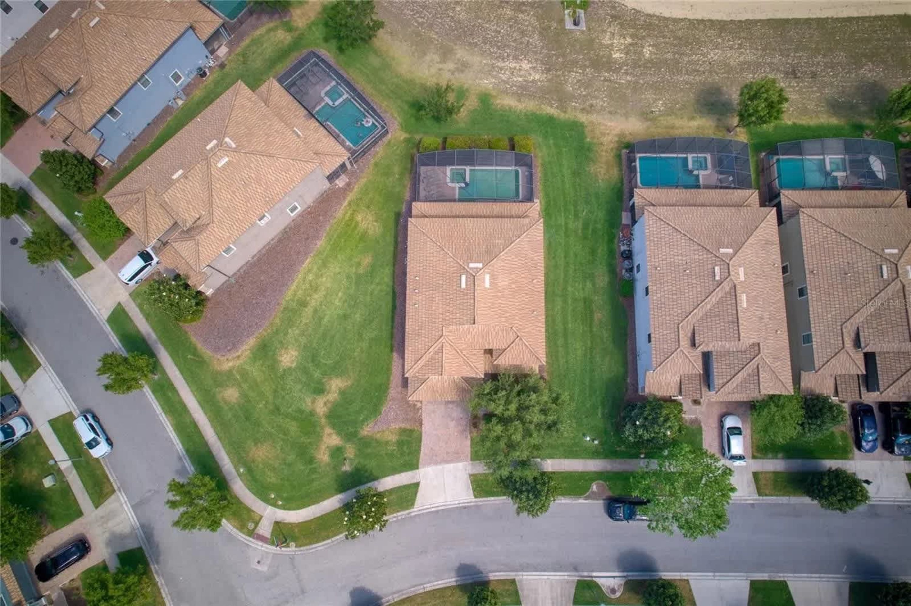 An aerial view of a residential area with houses featuring sloped roofs and swimming pools.