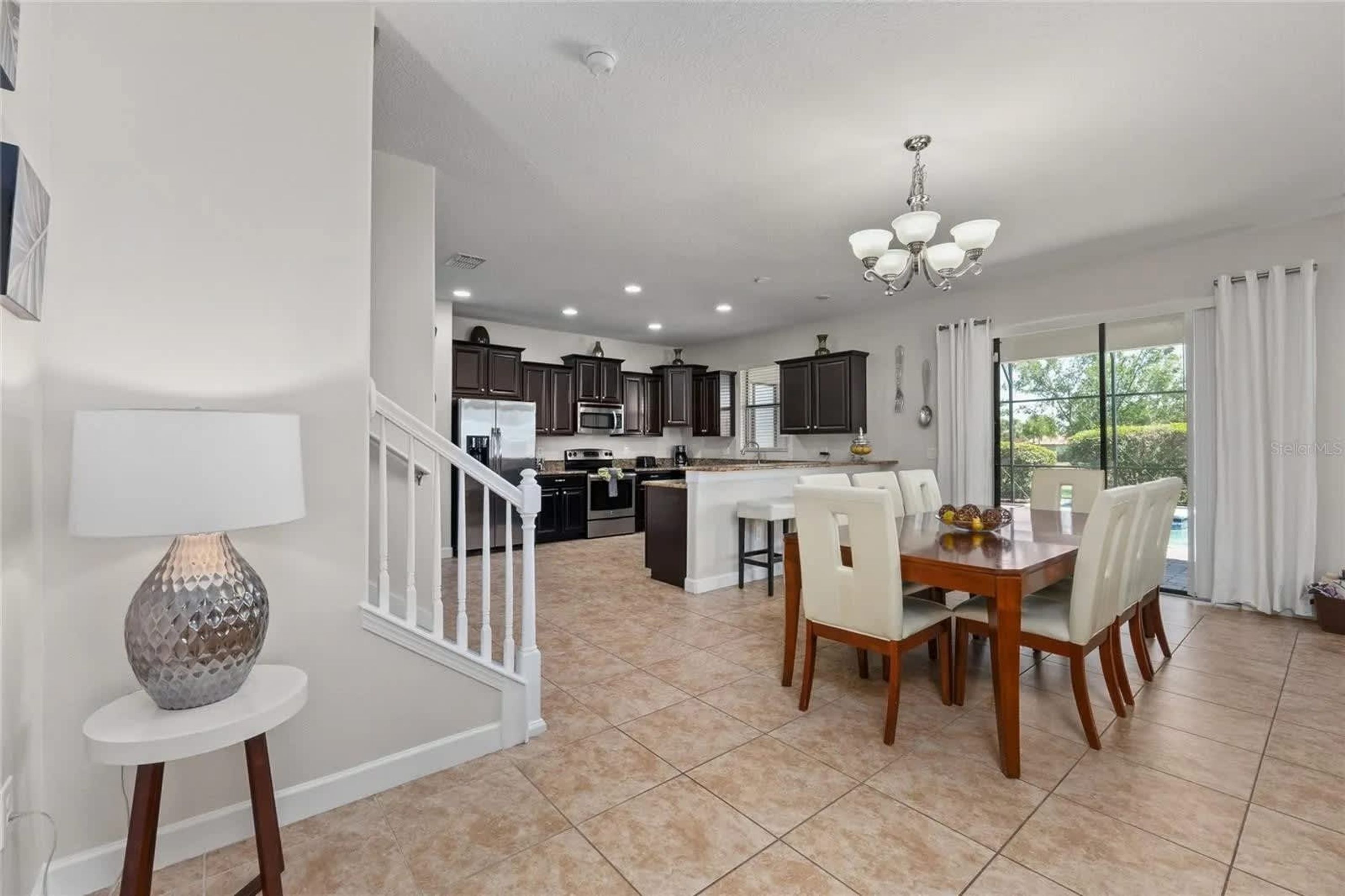 A modern kitchen with dark cabinets, a central island, and a dining area with a table and chairs.