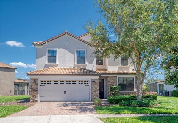 A two-story house with a white garage door, a stone facade, and a tiled roof.