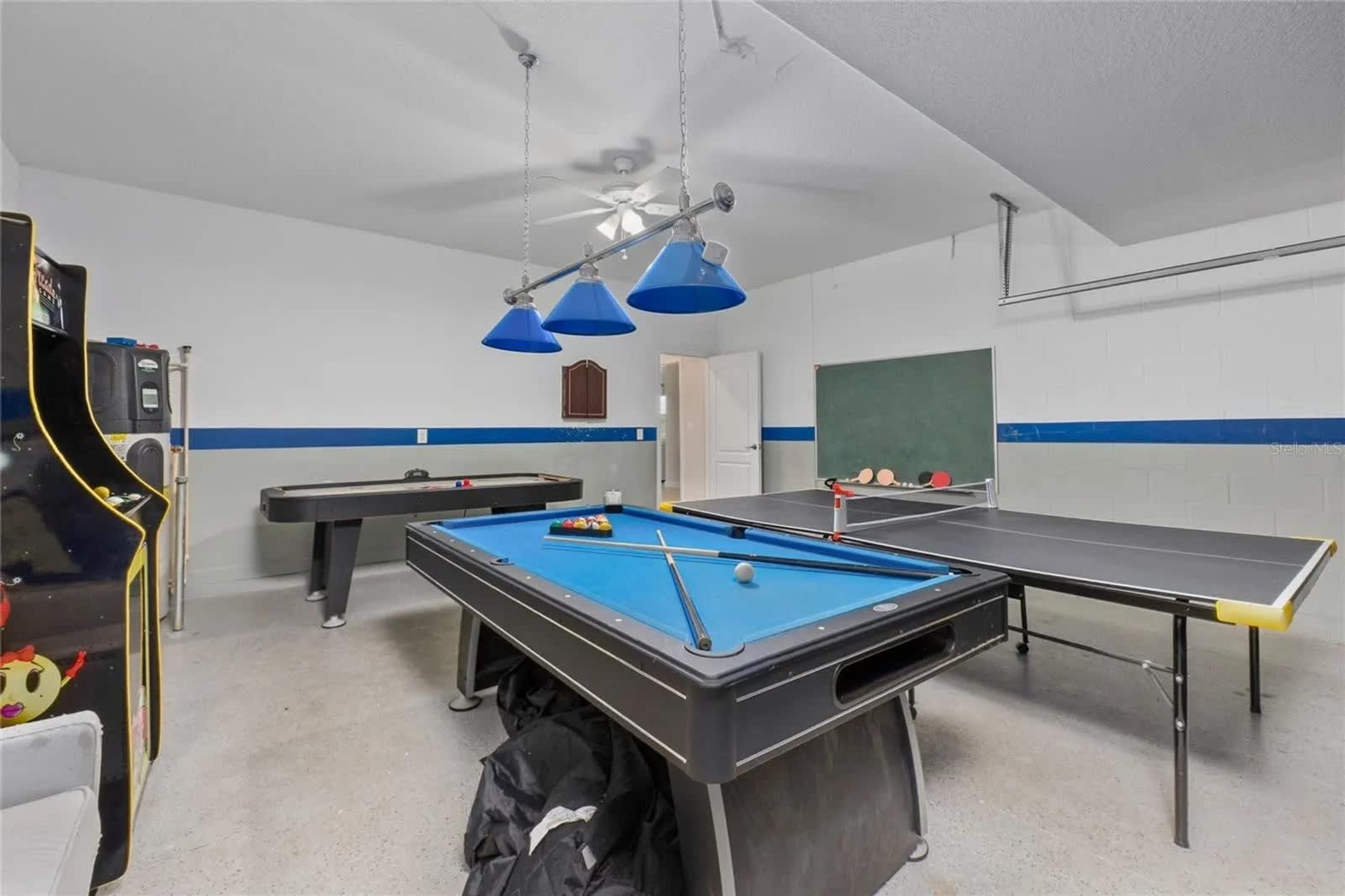 A pool table with blue felt, a ping pong table, and a billiards table in a room with white walls and blue trim.