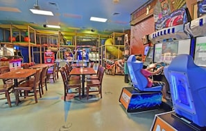 Ein Indoor-Spielbereich mit Spielautomaten, einer Rutsche und einem Essbereich mit Tischen und Stühlen.