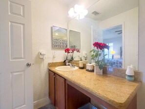 A bathroom with a sink, mirror, and two red flowers on the counter. - 4Br Resort Home With Pool and Lazy River Sleeps 8 (Davenport)