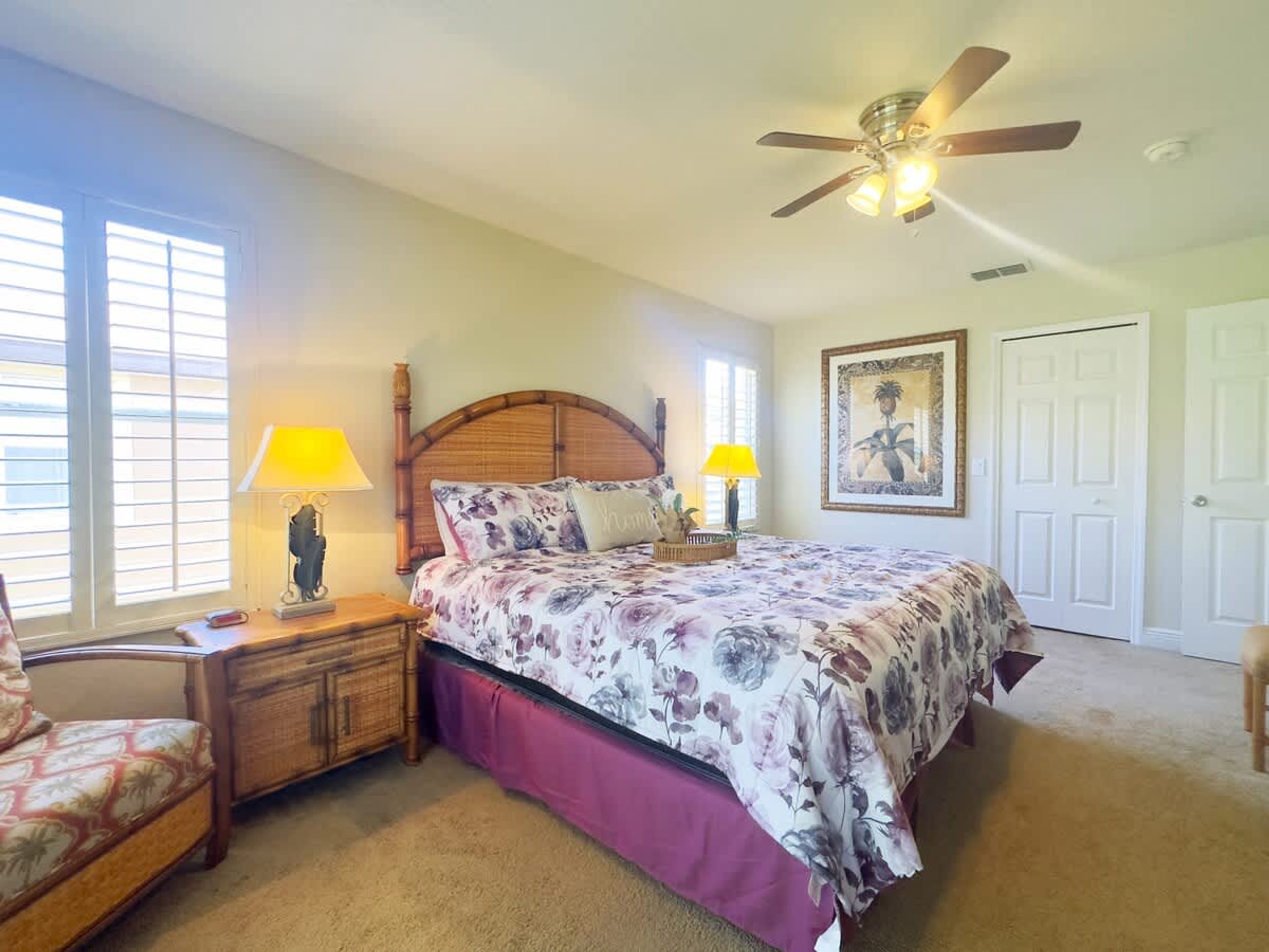 A bedroom with a bed, two nightstands with lamps, a ceiling fan, a door, and a window with blinds.