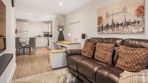 A modern living room with a brown leather sofa, a dining area with a white table, and a kitchen in the background. - Harmony 5 Mins to City Centre Balcony Fast Wifi (Coventry)