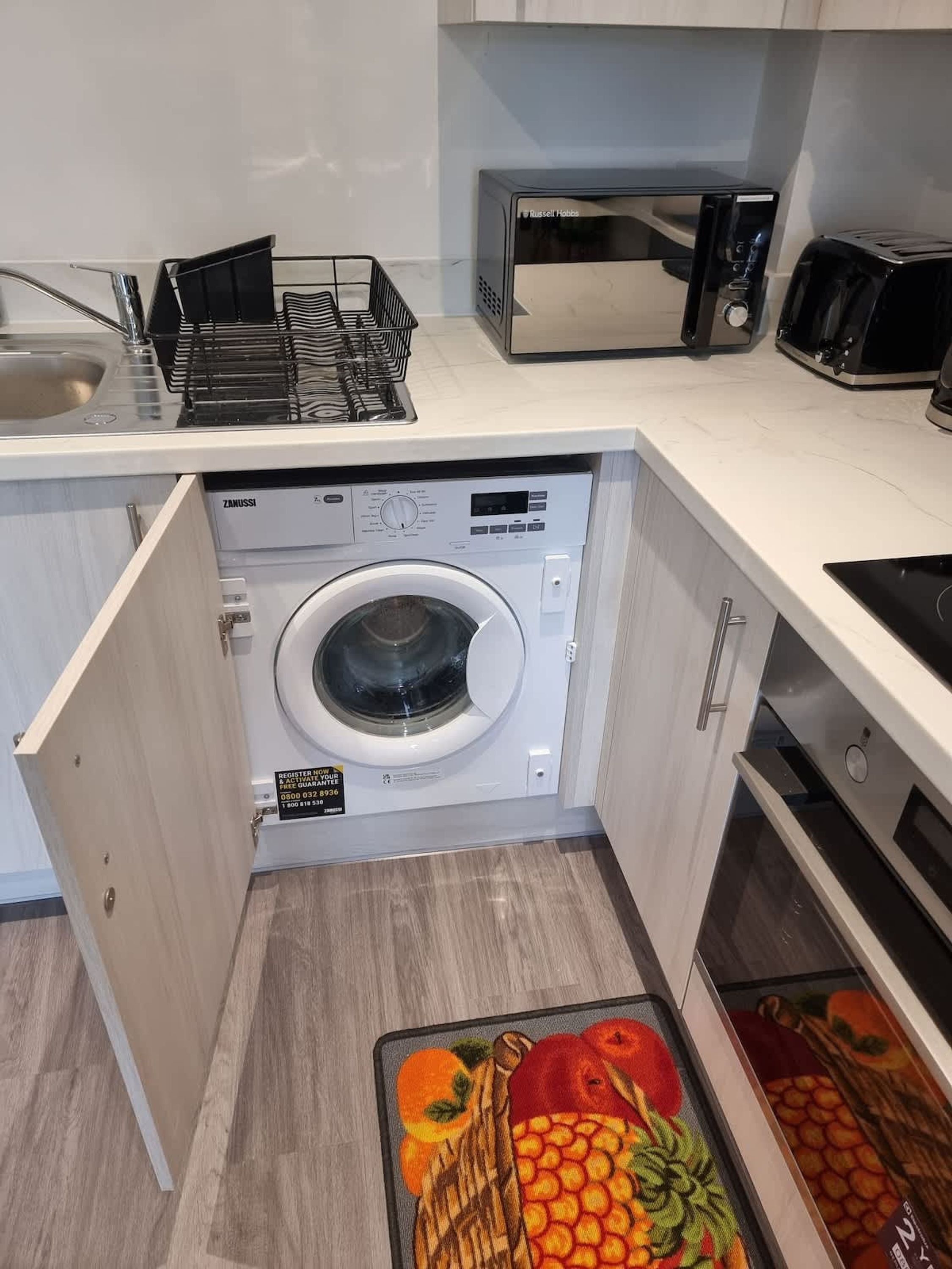 A compact kitchen with a built-in washer and dryer, a microwave, and a toaster.