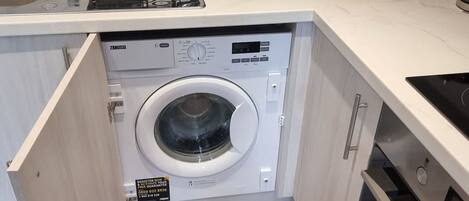 A compact kitchen with a built-in washer and dryer, a microwave, and a toaster.