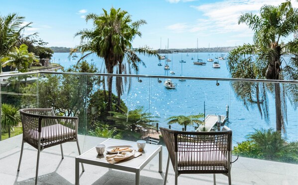 Un balcon agrémenté de chaises et d’une table en osier, donnant sur une marina où l’on peut admirer des bateaux et des palmiers.