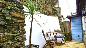A patio with a stone wall, a wooden table, two chairs, and a potted plant. - The Mermaid Loft in Cornwall (Tintagel)
