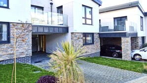 Une maison moderne à deux étages, dotée d’une façade en pierre, d’une allée couverte et d’une voiture garée dans le garage.