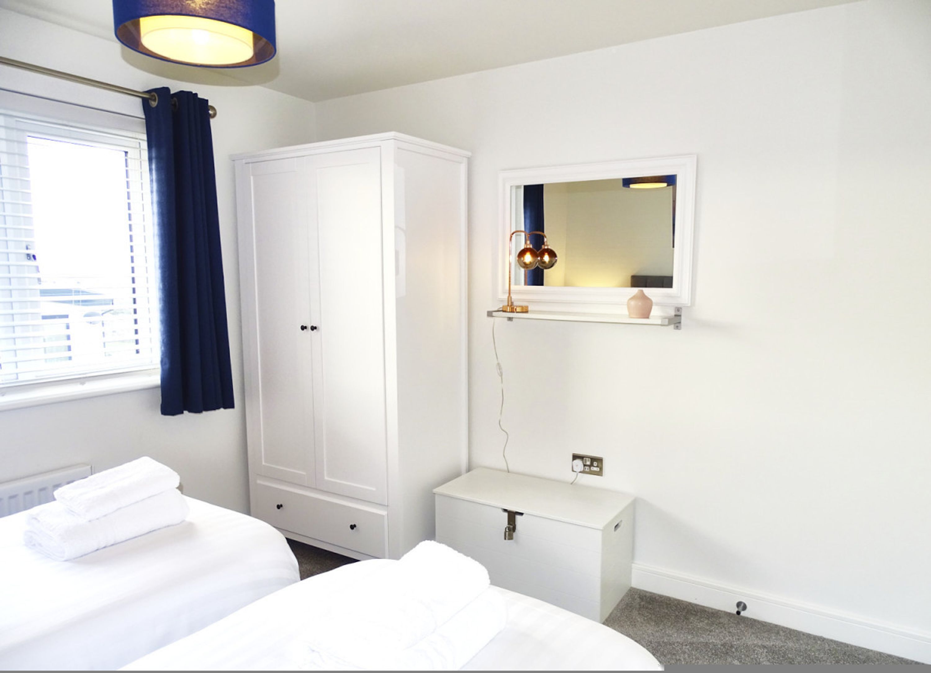 A bedroom with a bed, a wardrobe, a bedside table, a mirror, and a window with curtains.