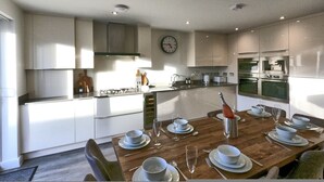 Une cuisine moderne avec des meubles blancs, une table à manger en bois mise avec des assiettes, des verres et des couverts, et une horloge au mur.