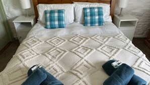 A bed with a wooden headboard, two matching pillows, a white quilt, and two bedside lamps on white nightstands. - The Stables in Crackington Haven (Bude)