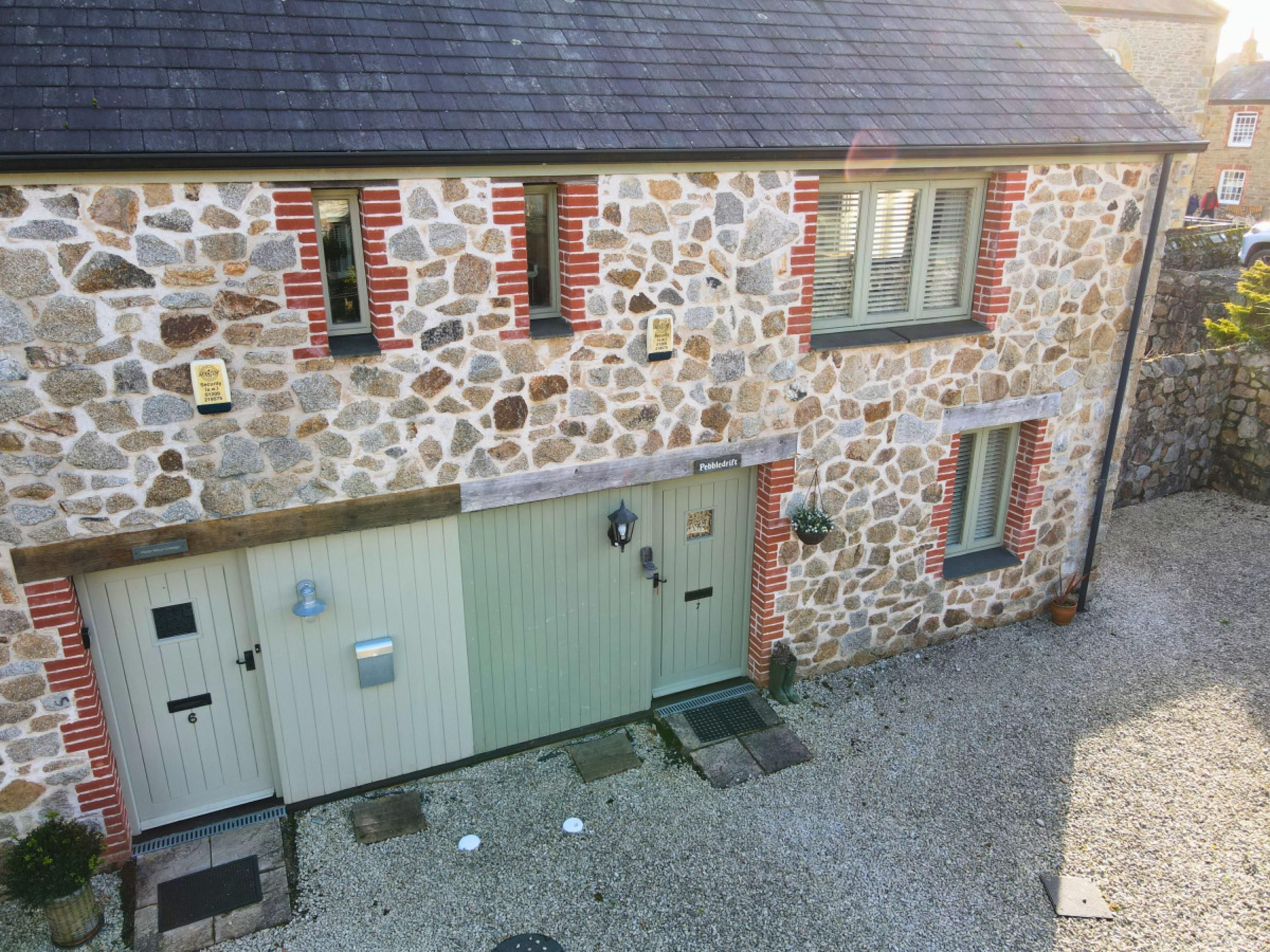 A stone building with a green door and windows, a gravel driveway, and a small garden area.