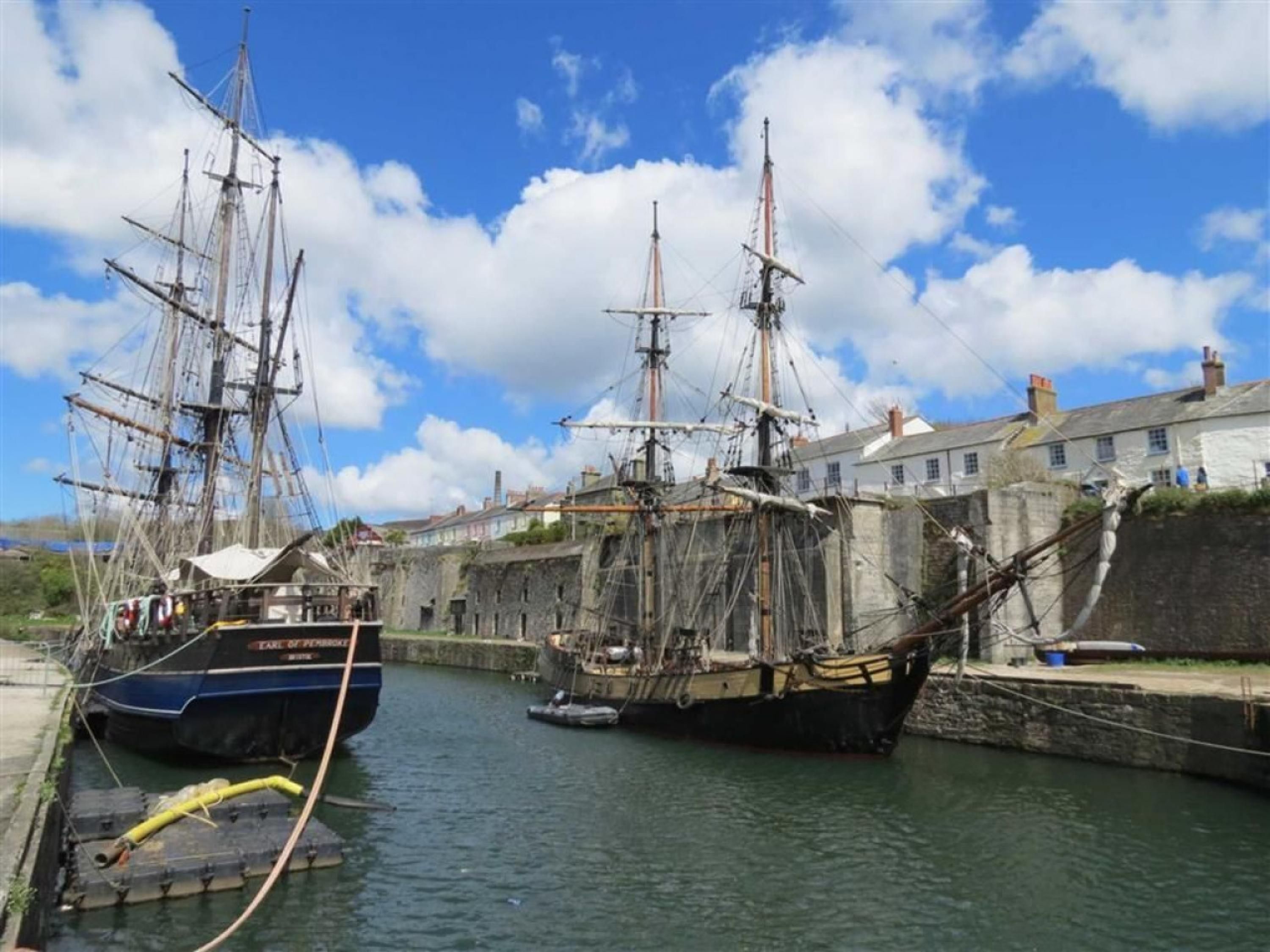 A harbor with two large sailing ships docked at a stone quay.