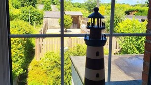 A model lighthouse on a windowsill with a view of a green landscape and buildings. - 8 Duke Street in Cornwall (Launceston)