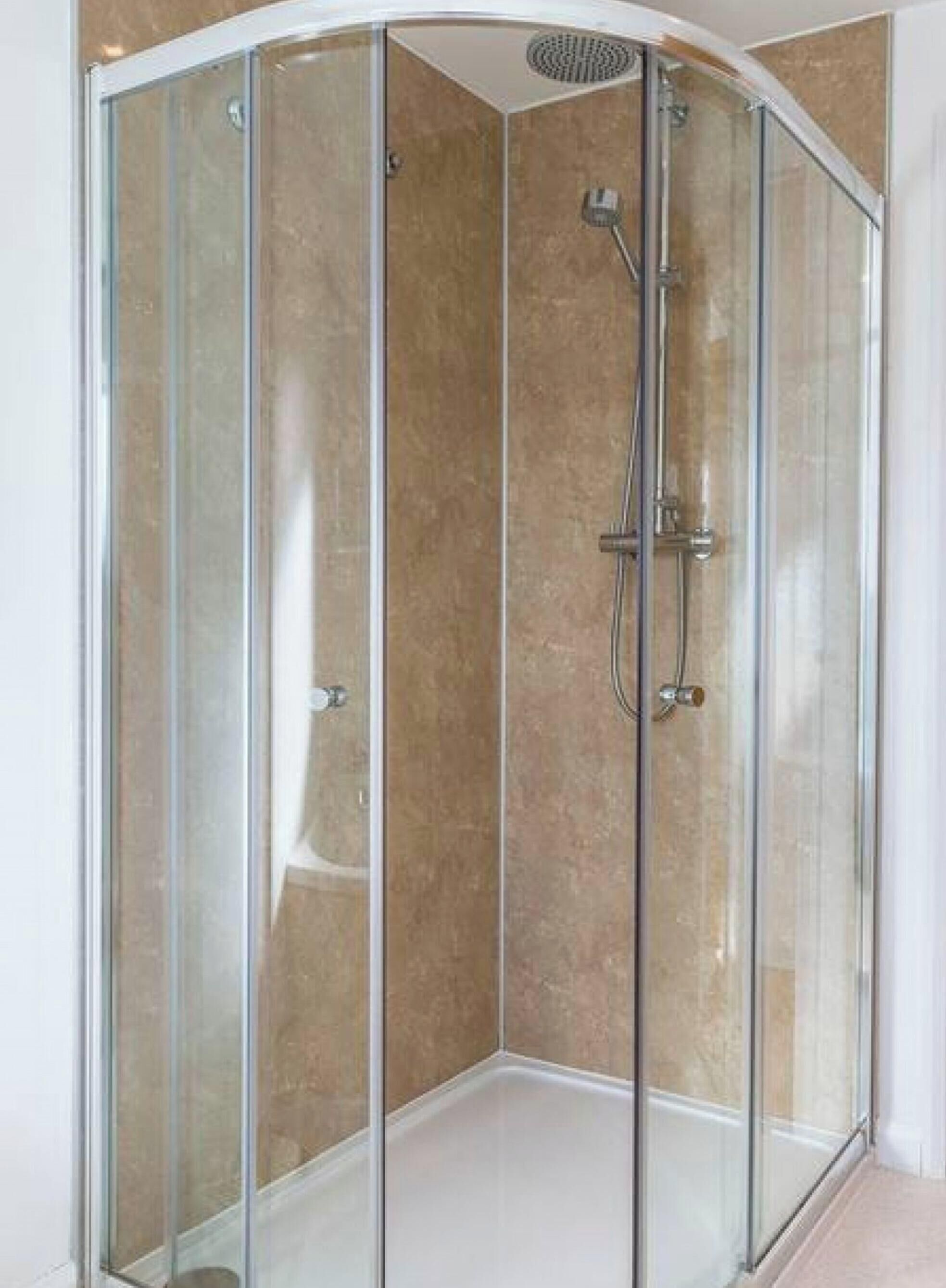 A glass-enclosed shower stall with a curved ceiling, a handheld showerhead, and a handheld shower control.