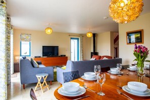 A modern living room with a sofa set, a dining table set for four, and a television. - Bay Retreat in Bude With 5 Bedrooms and 4 Bathrooms (Bude)