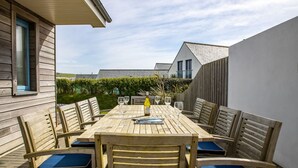 An outdoor wooden table with chairs, a bottle, and glasses on a patio.