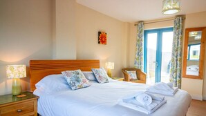 A hotel room with a large bed, two bedside tables, a nightstand, a chair, and a door with curtains.