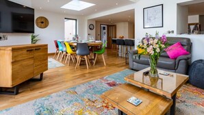 A modern living room with a wooden coffee table, colorful chairs, a grey sofa, and a flat-screen TV mounted on the wall. - Number 15 in Cornwall (Bude)