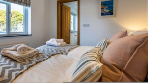 A hotel room with a bed, a window with curtains, a door, and a framed picture on the wall. - Number 15 in Cornwall (Bude)