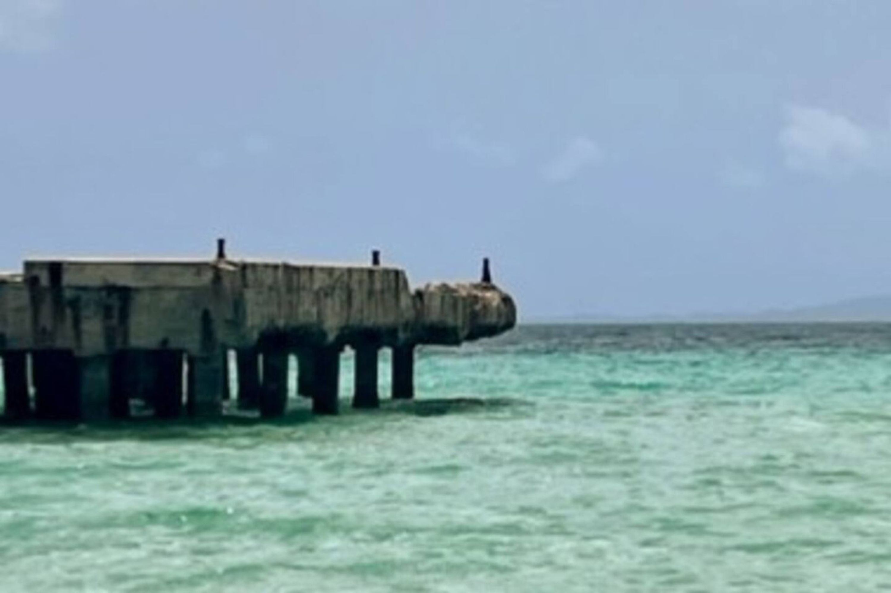A concrete pier extending into turquoise water with a clear sky above.