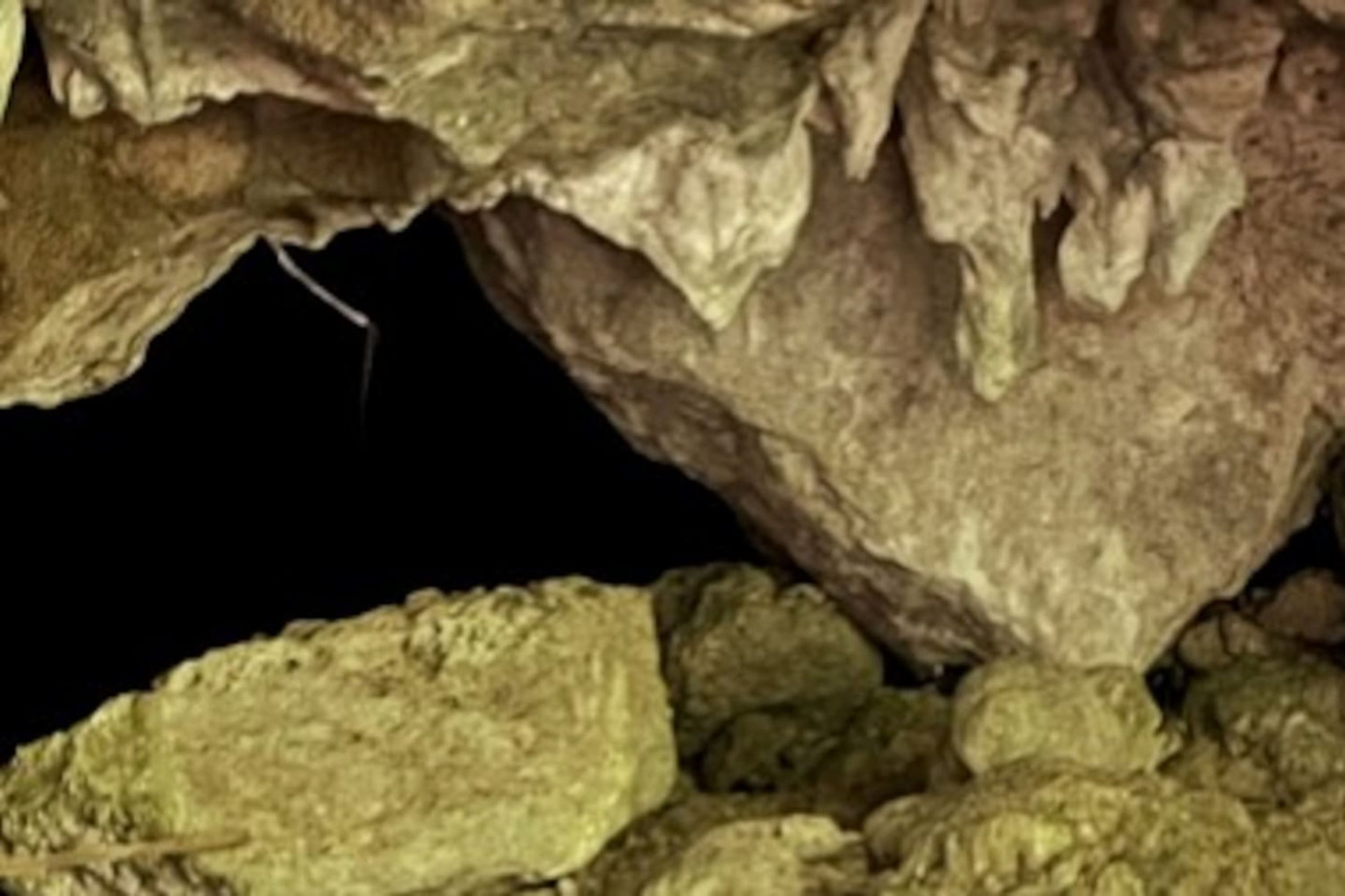 A cave interior with rough, uneven rock formations and stalactites.