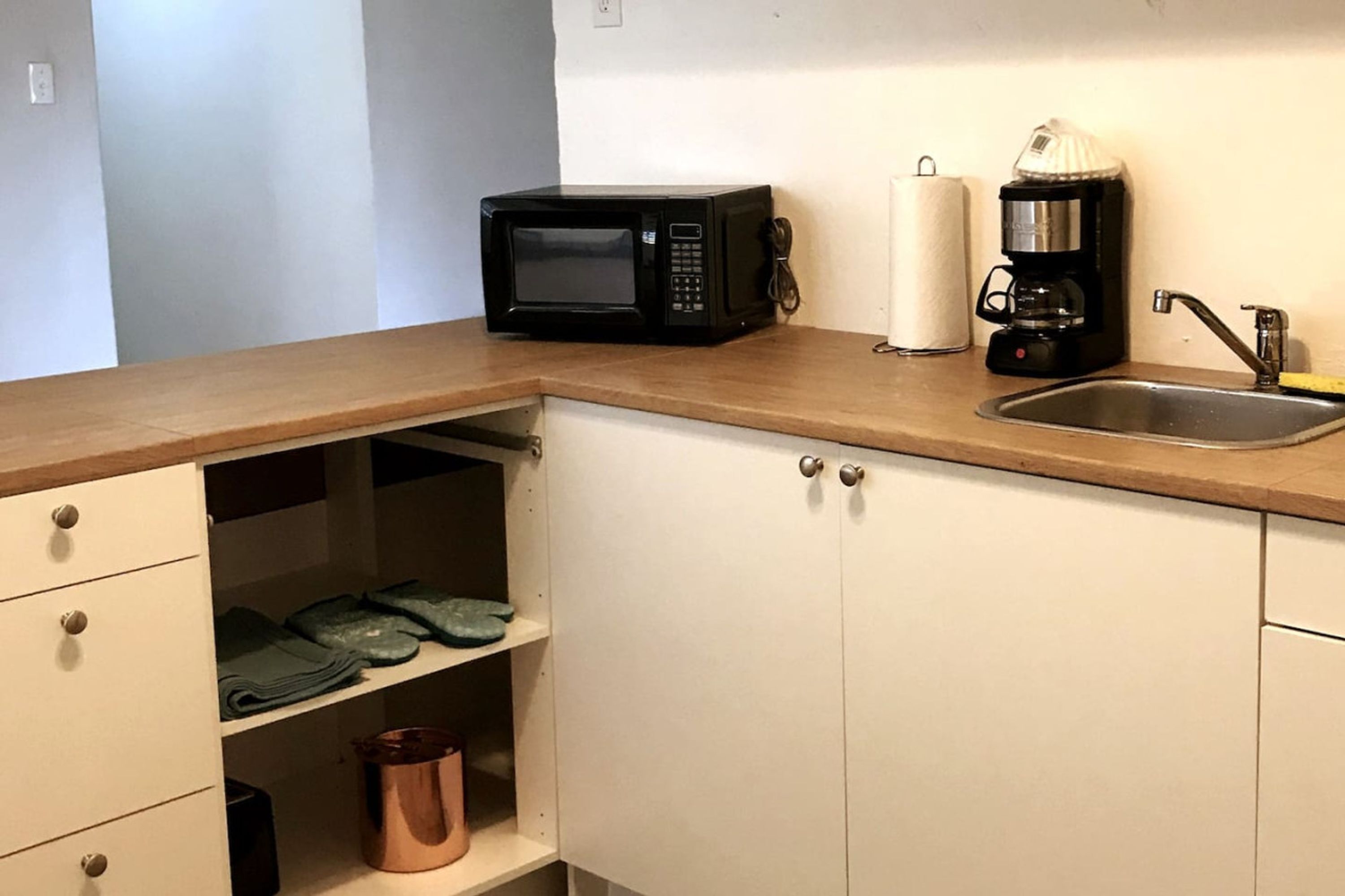 A kitchen with a microwave, coffee maker, and sink. There are cabinets with drawers and shelves.