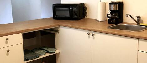 A kitchen with a microwave, coffee maker, and sink. There are cabinets with drawers and shelves.