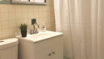 Un bany amb un lavabo blanc, un mirall a sobre, una planta en test i una cortina de bany.