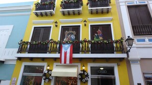 A yellow building with multiple balconies, some with plants. There is a flag in the center. - Casa del Sol-unit A Island Escape 3BR Near Hospital Malls (Bayamon)
