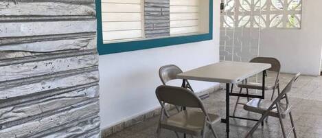 A room with a stone-textured wall, a window with blinds, a table with four chairs, and a patterned floor.