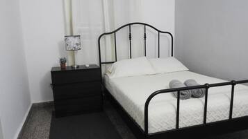 A single bed with a black metal frame, white bedding, and two rolled towels on the footboard.