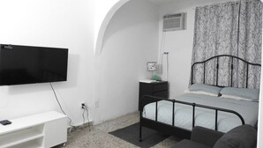 A bedroom with a bed, a TV mounted on the wall, a bedside table, and a small desk with a lamp. - Casa del Sol-unit A Island Escape 3BR Near Hospital Malls (Bayamon)