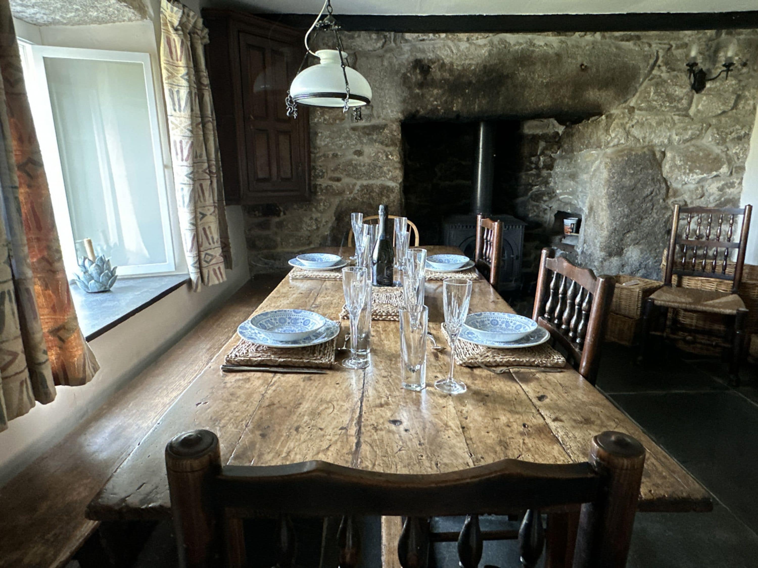 A rustic dining room with a wooden table set for six, flanked by stone walls and wooden chairs.
