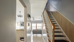 Un couloir menant à un escalier doté d’une rampe en bois et de marches blanches.