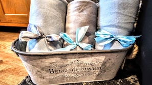 A metal bucket with the words 'Belle Jardiniere' and 'Rue du Pont-Neuf' engraved on it, containing rolled-up towels tied with blue ribbons. - Haycombe Farm Cottage (Camelford)