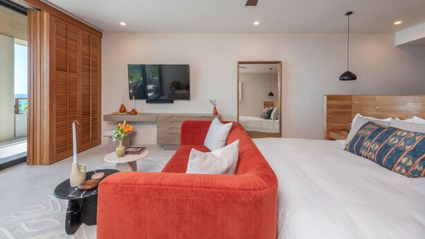 Une chambre moderne avec un grand lit, un canapé rouge, une télévision et un ventilateur de plafond.