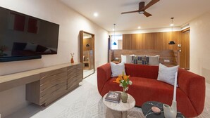 Un salon moderne avec un canapé rouge, une table basse surmontée d’un vase, un téléviseur fixé au mur et un ventilateur de plafond.
