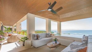 Un salon moderne doté d’une grande fenêtre donnant sur l’océan, d’un ventilateur de plafond et d’un coin salon confortable.