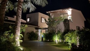 A modern building with a well-lit entrance, surrounded by palm trees and other greenery. - Villa Amada in Punta Mita (Punta de Mita)