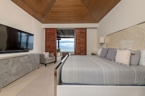 A modern bedroom with a large bed, a flat-screen TV, a grey dresser, and a view of the ocean through a sliding door. - PH Vista Ballena in Punta Mita (Punta de Mita)