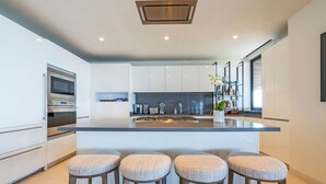 A modern kitchen with white cabinetry, a central island with bar stools, stainless steel appliances, and a large window providing natural light. - PH Vista Ballena in Punta Mita (Punta de Mita)