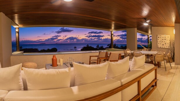 A modern outdoor seating area with a view of the ocean at sunset, featuring a wooden bench and a table with chairs. - Condo Haramara in Punta Mita (Punta de Mita)