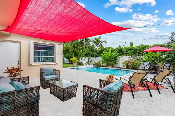 Un espace aménagé au bord de la piscine, avec des meubles en osier, un auvent rouge et une piscine.