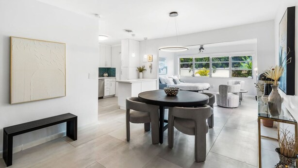 A modern kitchen with white cabinets, a dining area with a round table and chairs, and a large window with a view of greenery. - Oasis Backyard With Heated Pool Oakland Park (Wilton Manors)