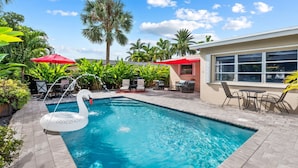A swimming pool with a swan float, surrounded by palm trees and outdoor furniture. - Oasis Backyard With Heated Pool Oakland Park (Wilton Manors)